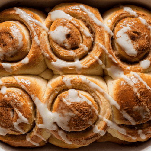 Apple Cinnamon Brioche Rolls 5 Golden-brown apple cinnamon brioche rolls drizzled with sugar glaze in a baking dish.